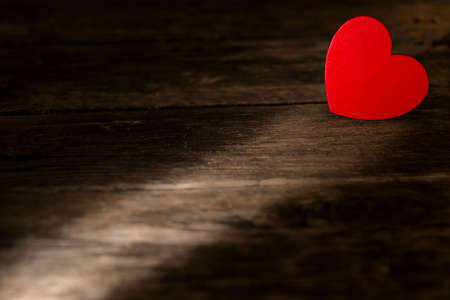 Minimalist composition of red heart lying on wooden table in beam of sunshineの写真素材