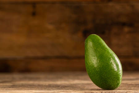 Closeup of bright ripe whole avocado with shiny peel composed on wooden tableの写真素材