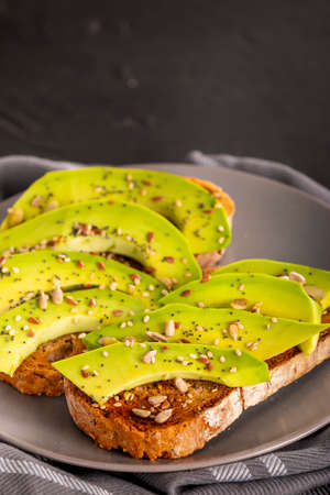 Plate of delicious sandwiches with slices of fresh avocado and spices placed on towel in kitchen
