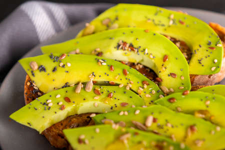 Plate of delicious sandwiches with slices of fresh avocado and spices placed on towel in kitchen