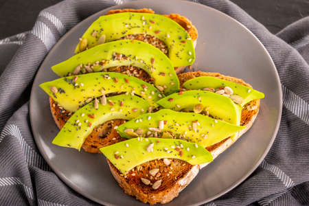 Plate of delicious sandwiches with slices of fresh avocado and spices placed on towel in kitchen