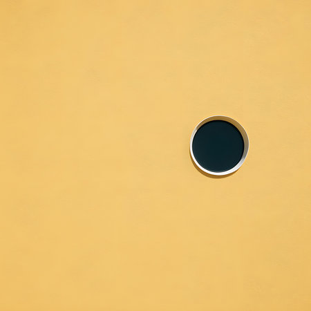 Round window on a yellow wall with a black hole in it.の素材