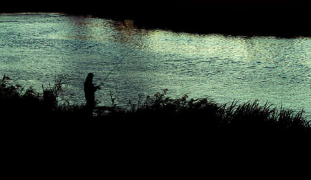 Fisherman's silhouette against the background of a small river on the sunsetの写真素材