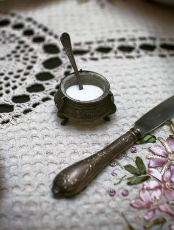 Vintage metal dishes: salt shaker and a knife on a white crocheted tableclothの写真素材