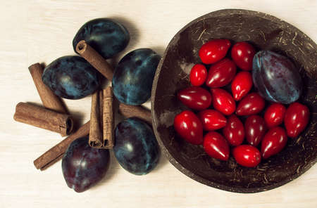Still life food with plums, red berries and cinnamon sticks in a coconut plate overhead on wooden backgroundの写真素材