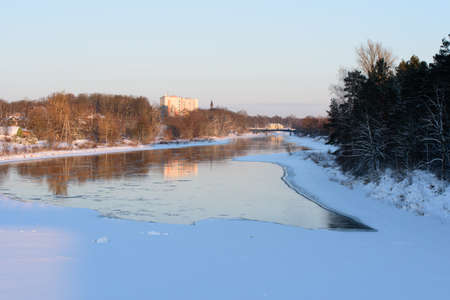 a beautiful sunset on an unfrozen river with snowy trees