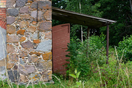 an old abandoned building in a nature park overgrown with grass on a cloudy day in the middle of summer with a brown wooden doorの写真素材