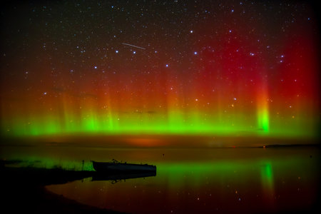 beautiful green red northern lights on the lake in autumn night with a lonely boatの写真素材