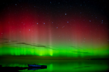 beautiful green red northern lights on the lake in autumn night with a lonely boatの写真素材
