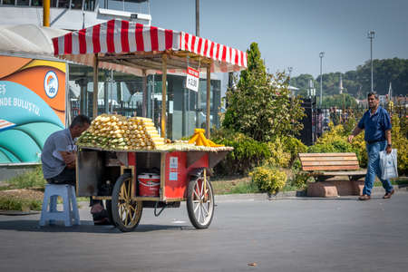 Istanbul, Turkey - September 05, 2015: Man is walking on the street near Eminonu port in Istanbul. Street vendor is selling corn, the price is 2 turkish lira per piece. That is typical fast food sold on the street in Istanbul, Turkeyのeditorial素材