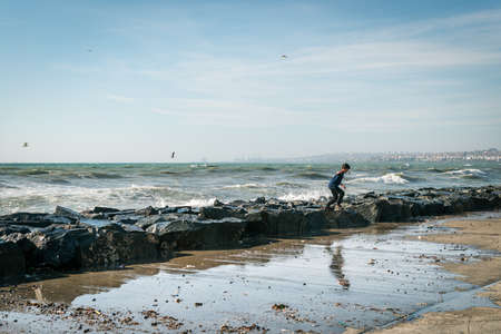 Istanbul, Turkey - November 22, 2015: Boy is playing next to the Sea of Marmara during the strong wind in Istanbul. Wavy seascape.のeditorial素材