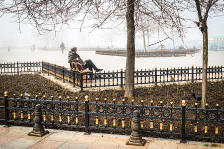 Istanbul, Turkey - February 29, 2016: Man is sitting on a bench in the park in Kadikoy. Deep fog over Istanbulのeditorial素材