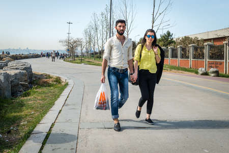 Istanbul, Turkey - April 17, 2016: Young couple is walking holding hands at seaside in Kadikoy,...