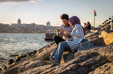 Istanbul, Turkey - April 25, 2016: Young turkish couple is sitting on the coast and using cellphone in Istanbul, Turkeyのeditorial素材
