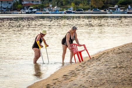 Porto Koufo, Chalkidiki, Greece - September 12, 2016: Two old ladies are getting out of the water near Porto Koufo at sunset in Greeceのeditorial素材