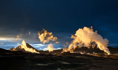 Steam erupting from geothermal power station at sunset, yellow light of setting sun back-lighting the columns of steam, Myvatn area, Icelandの写真素材