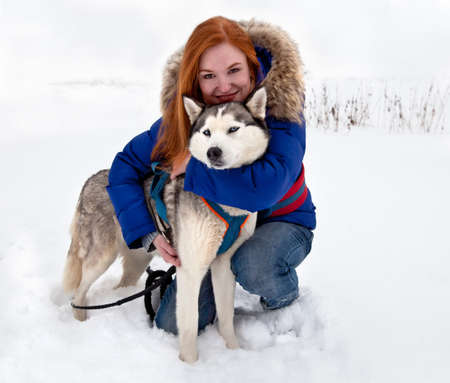 Young red-haired smiling woman and dog siberian husky in winterの写真素材