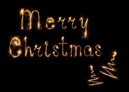 Sparkling burning Merry Christmas words and christmas tree on black background for design holiday web banner and greeting card. Words made by Bengal lights. Happy New Year theme.の写真素材
