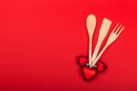 Wooden kitchen utensils with red hearts and empty space for text on red background. Cooking spoon,...