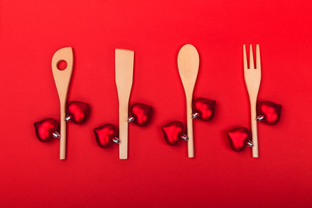 Wooden kitchen utensils with red hearts on red background. Cooking spoon, spatula and fork like branches and red hearts like leaves. Creative holiday kitchen concept on Valentines Day. Cooking with love. Top view, flat lay.の写真素材