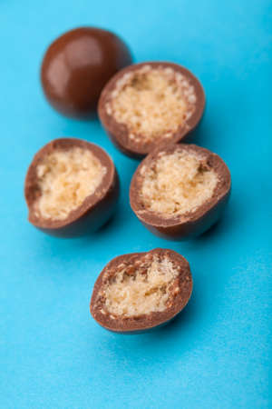 Close up of chocolate candy balls and halves with crispy corn filling on blue backgroundの写真素材