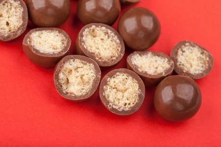 Close up of chocolate candy balls and halves with crispy corn filling on red backgroundの写真素材