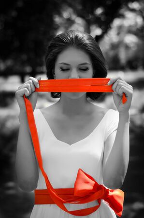 Black and white portrait of beautiful young girl with vivid red ribbon covering her mouth の写真素材
