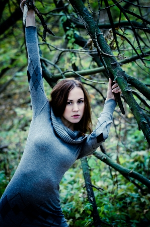 Young girl holding on to a branch in twilight forestの写真素材