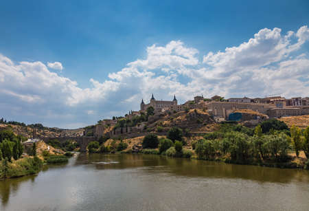 View of the old city and the Alcantara Bridge leading to the Gate of the Sun from the side of the River Tajo Toledo, Spain.の写真素材