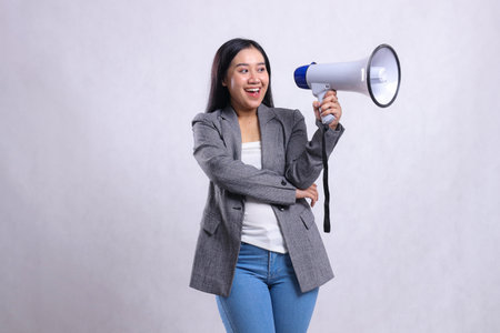 beautiful office woman asia screaming cheerful candid hugging holding megaphone loudspeaker wearing grey suit isolated on white background. for fashion, lifestyle, advertising, broadcast, shoppingの写真素材