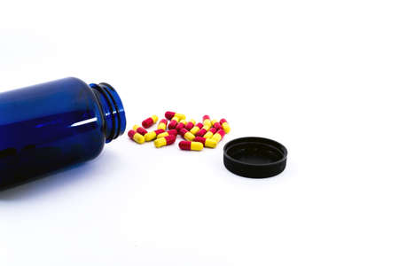 A group of capsule in red and yellow outside of bleu bottle and black cap isolated on white backgroundの写真素材