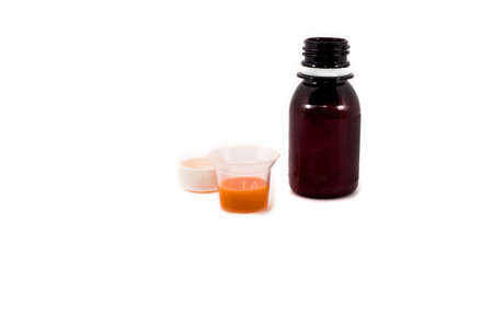 Medicine bottle with open cap and yellow msyrup medicine in transperant container isolated on white backgroundの写真素材