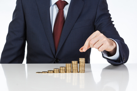 Businessman hand stacking one euro coins into increasing columns. Financial concept. Closeup.の写真素材