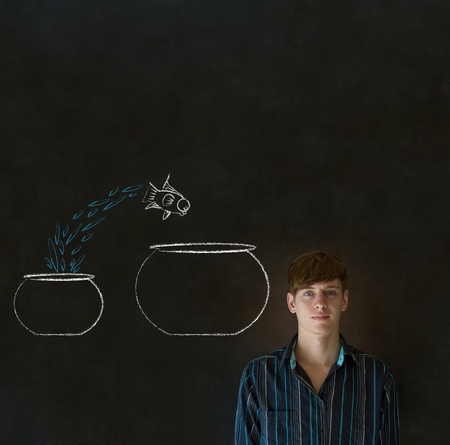 Business man, student or teacher with fish jumping from small bowl to big bowl on blackboard backgroundの写真素材