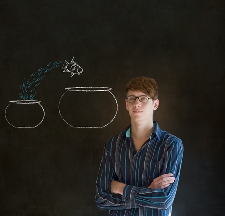 Business man, student or teacher with fish jumping from small bowl to big bowl on blackboard backgroundの写真素材