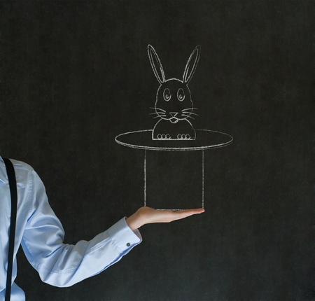 Business man, student or teacher pulling a rabbit from a magic hat on blackboard backgroundの写真素材