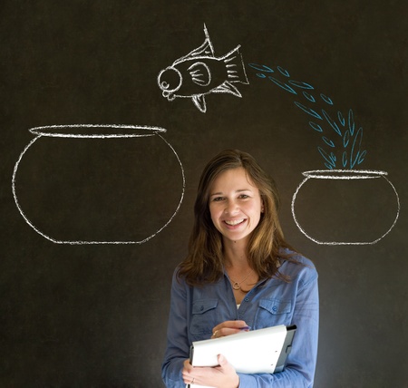 Business woman, student or teacher with fish jumping from small bowl to big bowl on blackboard backgroundの写真素材