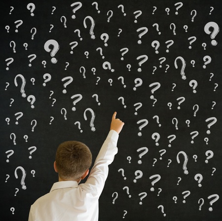 Hand up answer boy dressed up as business man with chalk questions marks on blackboard backgroundの写真素材