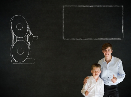 Thumbs up boy dressed up as business man with teacher man and retro chalk film projector on blackboard backgroundの写真素材