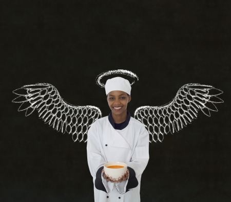 Woman female African or African American chef holding food soup bowl with angels wings and halo chalk blackboard backgroundの写真素材