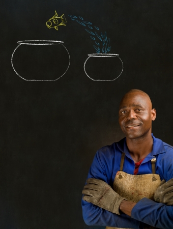 African American black man industrial worker with chalk jumping fish bowls on a blackboard backgroundの写真素材