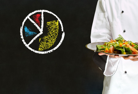 Chef holding salad platter with chalk pie chart on blackboard backgroundの写真素材