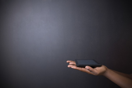 South African or African American woman teacher or student holding computer tablet on blackboard backgroundの写真素材