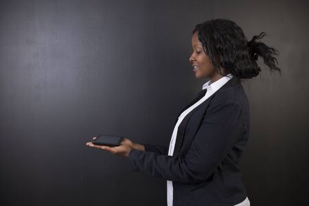 South African or African American woman teacher or student holding computer tablet on blackboard backgroundの写真素材