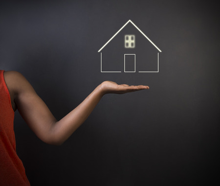 South African or African American woman teacher, student, saleswoman or businesswoman against black background holding house, home or real estateの写真素材