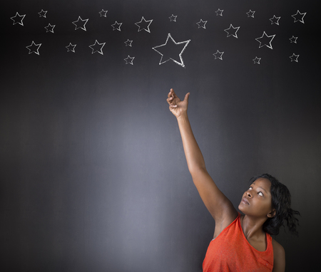 South African or African American woman teacher or student reaching for the stars success against blackboard backgroundの写真素材