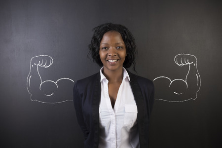 South African or African American woman teacher with healthy strong chalk arm muscles for success on blackboard backgroundの写真素材