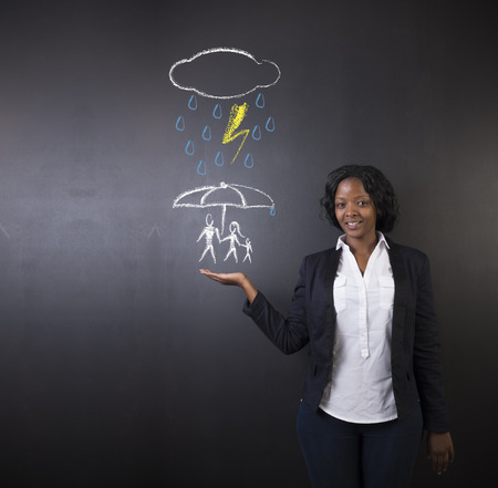 South African or African American woman teacher or student holding out her hand, displaying an insurance concept while thinking about protecting family from natural disaster on a blackboard backgroundの写真素材