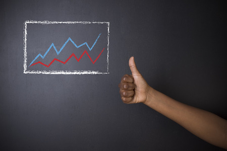 South African or African American woman teacher or student thumbs up against blackboard background with chalk growth line graphの写真素材
