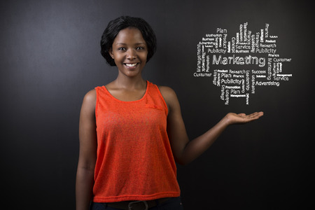South African or African American woman teacher or student standing with her hand out against a blackboard background with a chalk marketing diagramの写真素材
